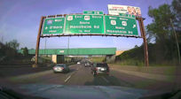 On-vehicle camera shows an overhead highway sign with exit information
